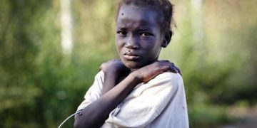 On 22 October 2016, a young girl, who has just arrived from Leer, where there is heavy fighting, poses for a photograph at the gate of  the  UN Protection of Civilian Camp (POC) Bentiu, South Sudan. Recent fighting  in Leer between Governemnt forces and rebel groups have forced thousands more people into the UN camp in Bentiu that is now home to 105,000 people.