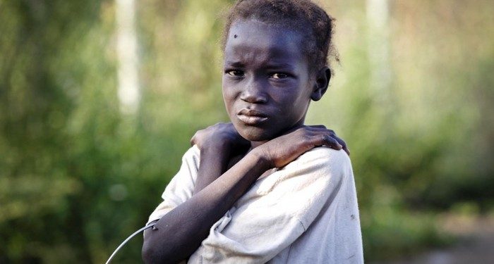 On 22 October 2016, a young girl, who has just arrived from Leer, where there is heavy fighting, poses for a photograph at the gate of  the  UN Protection of Civilian Camp (POC) Bentiu, South Sudan. Recent fighting  in Leer between Governemnt forces and rebel groups have forced thousands more people into the UN camp in Bentiu that is now home to 105,000 people.