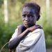 On 22 October 2016, a young girl, who has just arrived from Leer, where there is heavy fighting, poses for a photograph at the gate of  the  UN Protection of Civilian Camp (POC) Bentiu, South Sudan. Recent fighting  in Leer between Governemnt forces and rebel groups have forced thousands more people into the UN camp in Bentiu that is now home to 105,000 people.