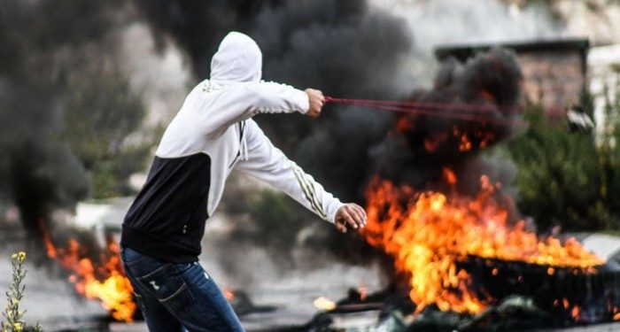 Ramallah, Palestinian Territory. 18th November 2012 -- A young man uses a slingshot as Palestinian protesters burn tires during clashes outside Ofer prison near the West Bank city of Ramallah following a protest against Israel's military operation in the Gaza Strip. -- Clashes between Palestinian youths and Israeli soldiers took place during a protest against Israel's operations in Gaza Strip, outside Ofer, an Israeli military prison near the West Bank city of Ramallah.