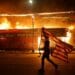 A protester carries a U.S. flag upside, a sign of distress, next to a burning building Thursday, May 28, 2020, in Minneapolis. Protests over the death of George Floyd, a black man who died in police custody Monday, broke out in Minneapolis for a third straight night. (AP Photo/Julio Cortez)