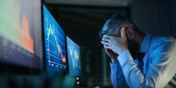 Frustrated and worried businessman with computer sitting at desk, working late. Financial crisis concept.