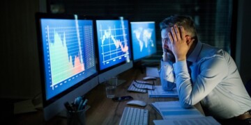 Frustrated and worried businessman with computer sitting at desk, working late. Financial crisis concept.