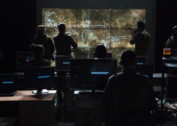 Group of soldiers or spies in dark room with large monitors and advanced satellite communication technology launching a missle. Includes flashing yellow light.