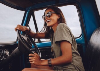 Portrait of young woman having fun while driving a car. Cheerful woman going on a road trip on a old truck.