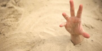 Hand sinking in quicksand, trying to get out, tips to survive in desert, buried