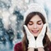 Outdoor close up photo of young beautiful happy smiling girl walking on street. Model closed her eyes and touching face, wearing stylish white knitted winter hat and gloves. Copy, empty space for text