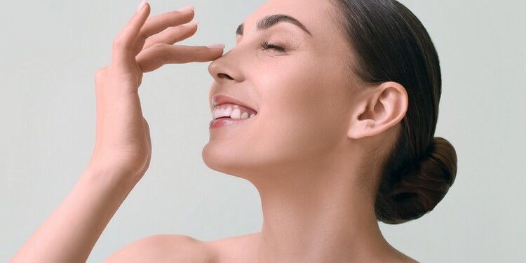 Young woman with healthy skin touching nose on color background