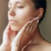 Cropped shot of young caucasian woman touching skin with hands massaging her face isolated on a dark brown background. Rejuvenation, facelift, facefitness. Cosmetology and beauty concept