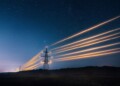 Electricity transmission towers with orange glowing wires the starry night sky. Energy infrastructure concept.