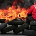 Flames and smoke rise from burning tyres as a worker sits on a barricade blocking the entrance of U.S. tyre-maker Goodyear's plant to protest job cuts in Amiens, northern France, in this June 3, 2013 file picture. French trade unionists held two executives overnight on Tuesday January 7, 2014 at the country's Goodyear tyre plant - a flashpoint for France's troubled industrial relations - to demand higher pay-outs for more than a thousand planned layoffs. Workers at the idled factory in the northern city of Amiens have been trying to negotiate redundancy terms with management for nearly a year, after Texan tyre tycoon Maurice Taylor withdrew a potential rescue bid on the grounds that French workers were lazy - triggering a political storm.  The message reads "Goodyear - Gangster Bosses".  Picture taken June 3, 2013.  REUTERS/Benoit Tessier/Files  (FRANCE - Tags: BUSINESS INDUSTRIAL EMPLOYMENT)