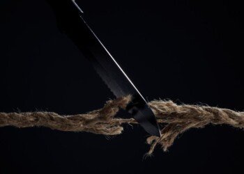 Horizontal shot of stretched cord is cut with a knife on a dark background. The rope is about to break. The concept of the danger of rupture.