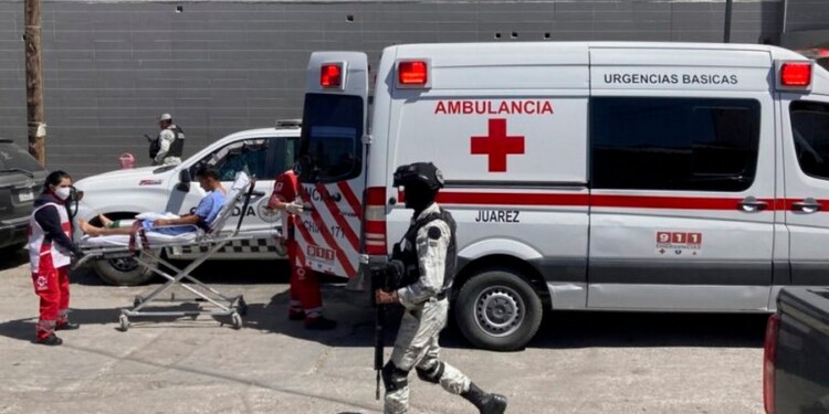 A security officer walks past as the Red Cross loads a patient, injured in a migrant detention center fire, into an ambulance, Tuesday, March 28, 2023, at a hospital in Cuidad Juarez, Mexico. According to Mexican President Andres Manuel Lopez Obrador, migrants fearing deportation set mattresses ablaze at the center, starting the fire that killed at least 40 migrants. (AP Photo/Morgan Lee)