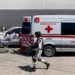 A security officer walks past as the Red Cross loads a patient, injured in a migrant detention center fire, into an ambulance, Tuesday, March 28, 2023, at a hospital in Cuidad Juarez, Mexico. According to Mexican President Andres Manuel Lopez Obrador, migrants fearing deportation set mattresses ablaze at the center, starting the fire that killed at least 40 migrants. (AP Photo/Morgan Lee)