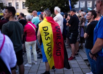 A man covering with a German national flag with the slogan "We are the people" listens to Bjoern Hoecke, top candidate of the far-right Alternative for Germany party, or AfD, during an election campaign rally of the party for upcoming state elections in Suhl, Germany, Tuesday, Aug. 13, 2024. (AP Photo/Markus Schreiber)