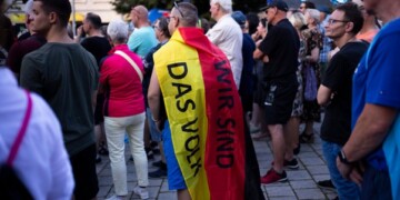 A man covering with a German national flag with the slogan "We are the people" listens to Bjoern Hoecke, top candidate of the far-right Alternative for Germany party, or AfD, during an election campaign rally of the party for upcoming state elections in Suhl, Germany, Tuesday, Aug. 13, 2024. (AP Photo/Markus Schreiber)