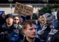 Police officers stand next to demonstrators with a sign "no Friedrich, the AfD is no alternative" during a protest against an AfD election campaign in Neu Isenburg near Frankfurt, Germany, Saturday, Feb. 1, 2025. (AP Photo/Michael Probst)