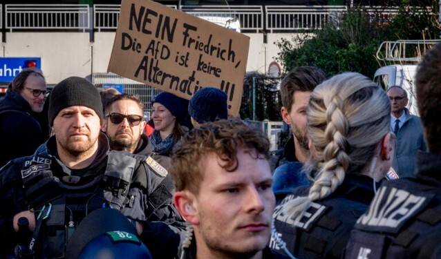 Police officers stand next to demonstrators with a sign "no Friedrich, the AfD is no alternative" during a protest against an AfD election campaign in Neu Isenburg near Frankfurt, Germany, Saturday, Feb. 1, 2025. (AP Photo/Michael Probst)