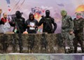 Israeli hostages Averu Mengistu (4th-R) and Tal Shoham (L) are flanked by Hamas fighters as they stand on a stage during their release in Rafah in the southern Gaza Strip on February 22, 2025. Masked militants paraded Tal Shoham and Averu Mengistu on stage in the southern Gazan city of Rafah before handing them over to officials from the Red Cross. (Photo by Omar AL-QATTAA / AFP)