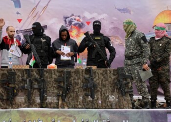 Israeli hostages Averu Mengistu (4th-R) and Tal Shoham (L) are flanked by Hamas fighters as they stand on a stage during their release in Rafah in the southern Gaza Strip on February 22, 2025. Masked militants paraded Tal Shoham and Averu Mengistu on stage in the southern Gazan city of Rafah before handing them over to officials from the Red Cross. (Photo by Omar AL-QATTAA / AFP)