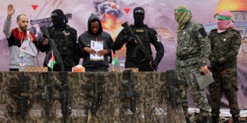 Israeli hostages Averu Mengistu (4th-R) and Tal Shoham (L) are flanked by Hamas fighters as they stand on a stage during their release in Rafah in the southern Gaza Strip on February 22, 2025. Masked militants paraded Tal Shoham and Averu Mengistu on stage in the southern Gazan city of Rafah before handing them over to officials from the Red Cross. (Photo by Omar AL-QATTAA / AFP)